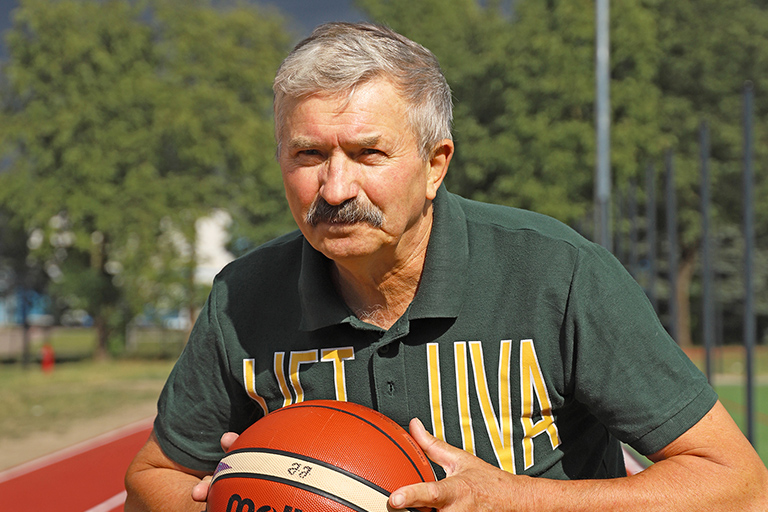 Natural Pharmaceuticals Movisan™ Collagen II Vyresnis vyras su ūsais laiko krepšinio kamuolį lauko aikštelėje su žaliais medžiais fone.