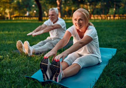 Natural Pharmaceuticals Movisan™ Collagen II Vyresnio amžiaus pora atlieka tempimo pratimus lauke ant kilimėlių žolėje saulėtu oru.